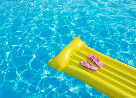 Beach summer holiday background. Inflatable air mattress, flip flops and hat on swimming pool.の写真素材