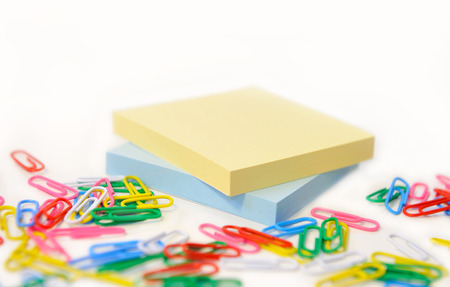 Small pads in different colors for records on background multicolored paper clips on white.