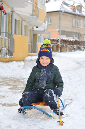 Little boy sitting on a sled in the yard of a house.の写真素材