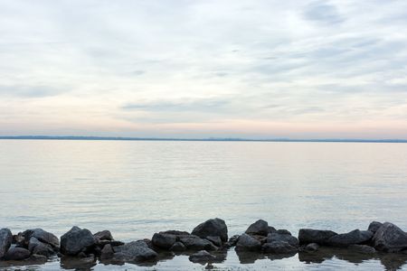 Horizontal theme by means of stones, water, skyline, and sky during dramatic sunset over lake Garda