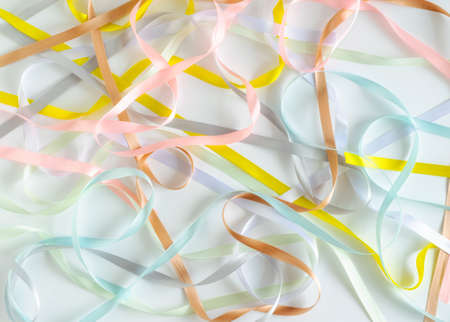 Satin narrow ribbons of pink, white, gray, brown, blue and yellow colors are randomly scattered on a white background. Wallpaper.Abstract background.の写真素材