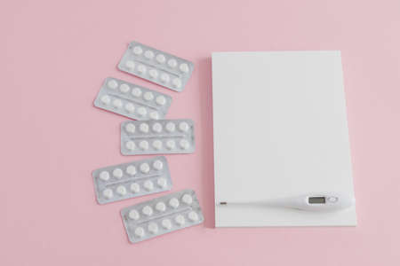 Blank white notepad with thermometer for measuring body temperature and a scattering of blisters...