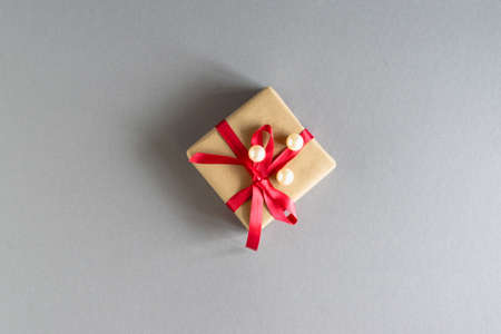 On a gray background, a gift in craft packaging with a red ribbon and white beads. Layout.