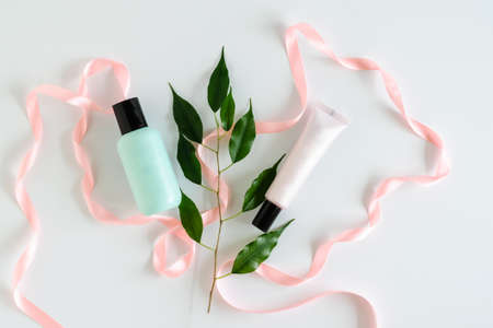 Empty bottles for cosmetics on white background with pink satin ribbon and green leaves. Natural cosmetics and ecology concept. Mock upの写真素材