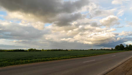 Sunset over the road between fields and meadows. Beautiful clouds. Horizontal photo.