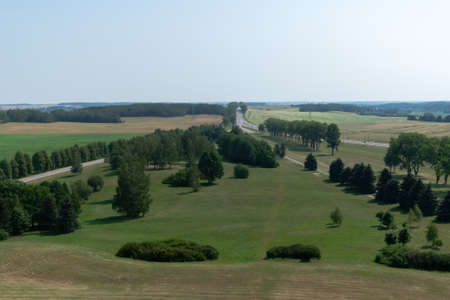 Top view of a plain with green meadows with parklands and a highway with passing cars. Horizon....