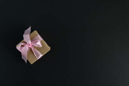 Against a dark background, a gift wrapped in craft paper is tied with a pink satin ribbon. The concept of the holiday and congratulations.の写真素材