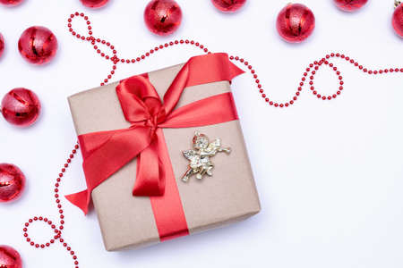 On a white background, a gift with a red ribbon and an angel next to the red Christmas balls....