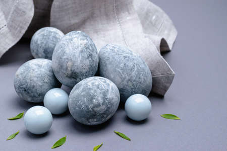 Close-up of marble-colored Easter eggs with green leaves and a napkin on a gray background. Easter...