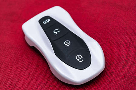 Close-up of a white-black smart car key on a red embossed background. Electronics, spare parts and car accessories. horizontal photo.の写真素材
