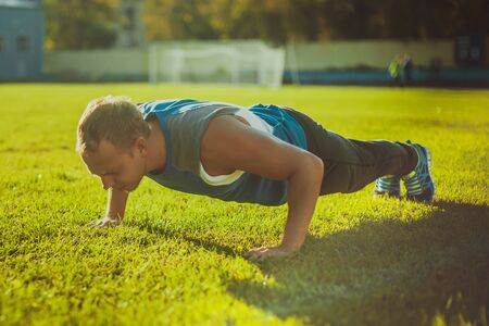 sport man stretching at the park, doing doing push-ups on  grass on a sunny day. Fitness conceptsの写真素材