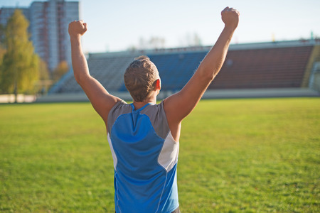 Athletic man is happy and rejoicing at the stadium, raised his hands up. Winnerの写真素材
