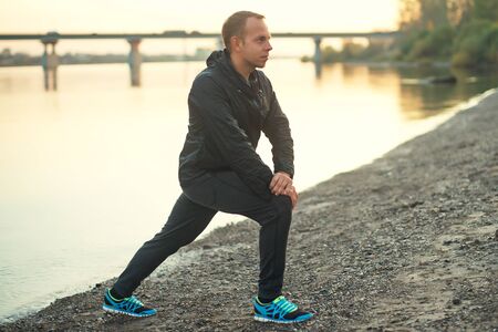 Athletic man doing exercise on the beach at sunset outdoors.の写真素材