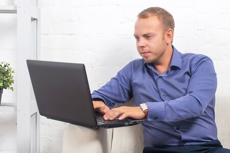 Handsome businessman sitting on couch with laptop at home in the living room, looking cameraの写真素材