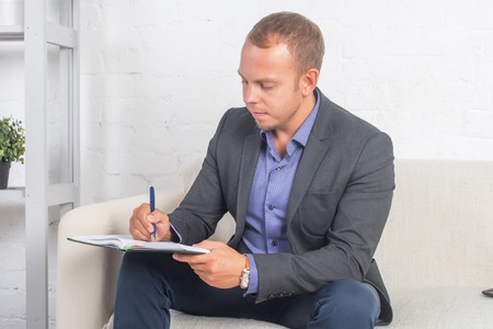 Handsome businessman sitting on couch with notebook at home in the living room, looking cameraの写真素材