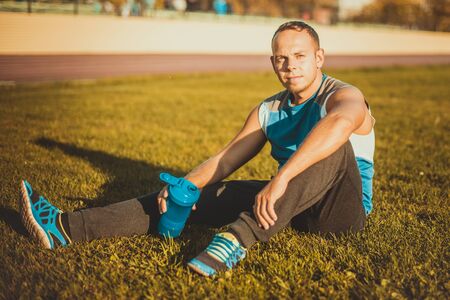 Sporting an attractive man sitting on the grass and rests in the stadium and keeps the shaker on sunny dayの写真素材