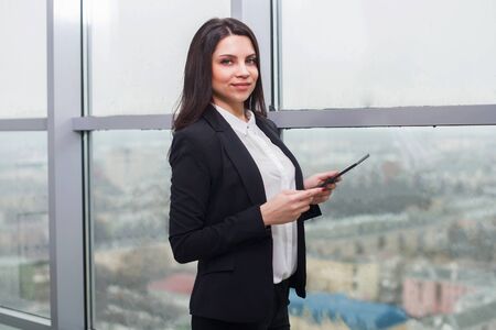 Young beautiful business woman standing at window with tablet.の写真素材