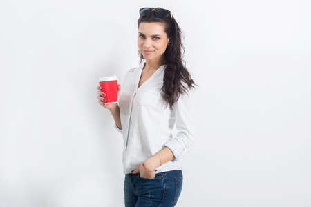 Beautiful young woman posing in jeans on a white wall with a takeaway coffee.の写真素材