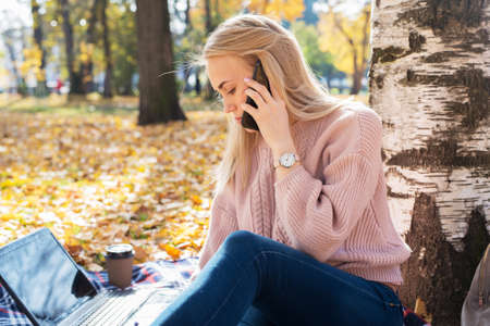 Young woman working with laptop outdoors and holding phone.の写真素材