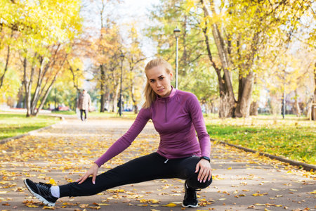 Young woman does stretching exercises in the park. Sports outside in autumn.の写真素材