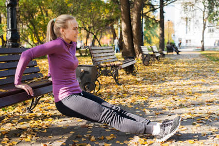 Young woman does push-up exercises in the park. Sports outside in autumn.