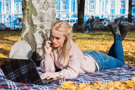A young woman works in a park, typing on a laptop.の写真素材