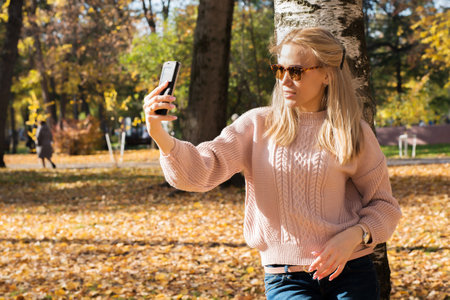 Selfie portrait of a happy young woman outside in the autumn park.の写真素材