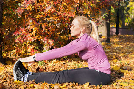 Young woman does stretching exercises in the park. Sports outside in autumn.の写真素材