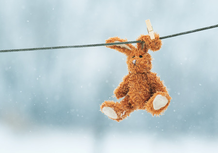 sad little toy rabbit hanging from a rope in the snowの写真素材
