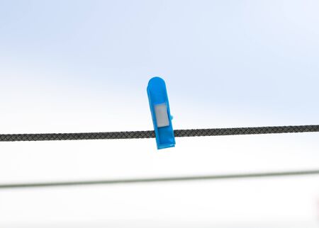 blue plastic clothespin hanging on a rope on sky backgroundの写真素材