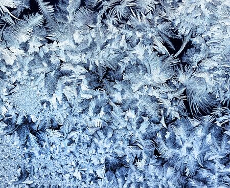 festive background from a shiny frosty pattern with beautiful intricate coils on glass in winter