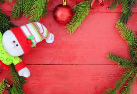 festive background of fragrant green fir tree branches , Christmas ball and a funny snowman on a red wooden tableの写真素材