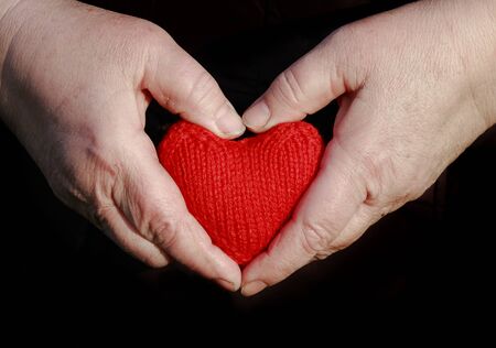hands of an elderly female pensioner holding carefully knitted red heartの写真素材