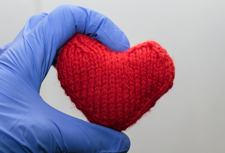 warm knitted red heart holding a hand in medical gloves