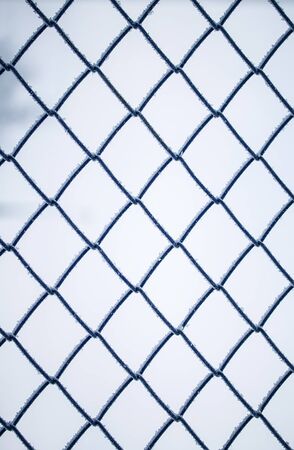 background of square blue metal grill netting covered with fluffy white crystals of frostの写真素材