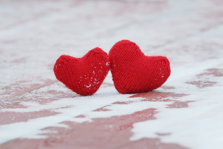 the symbol of love two red warm knitted hearts lie together on a wooden table under the snowの写真素材