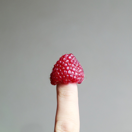 bright delicious juicy raspberry dressed as a cap on your fingerの写真素材