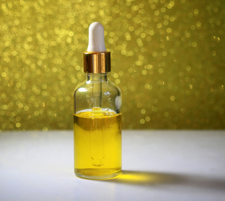 bright yellow beauty cosmetic oil stands in clear vial with dropper on table on Golden backgroundの写真素材