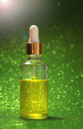 bright Golden cosmetic oil for beauty is in a transparent bottle with eye dropper brilliant green festive background Sunnyの写真素材