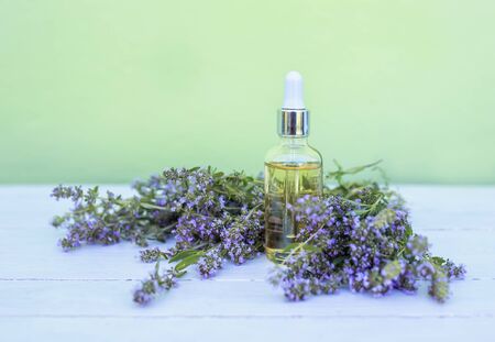 glass bottle with cosmetic oil stands on a wooden white table with delicate lilac thyme flowersの写真素材