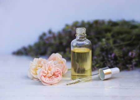 bottle with cosmetic rose oil and a pipette stands on a wooden table in delicate lavender colors outsideの写真素材