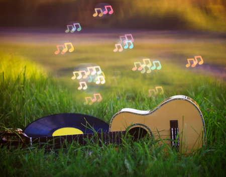 background with music a wooden guitar and a vinyl record lie in the green grass and shiny notes sounds fly over itの写真素材