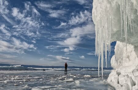man looks at the beautiful clouds over the ice of lake Baikalの写真素材