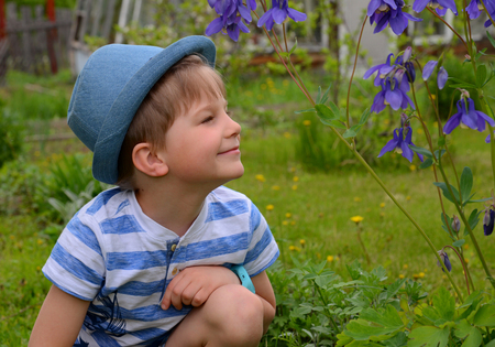a boy in a blue hat sits in a meadow and looks at a flowerの写真素材