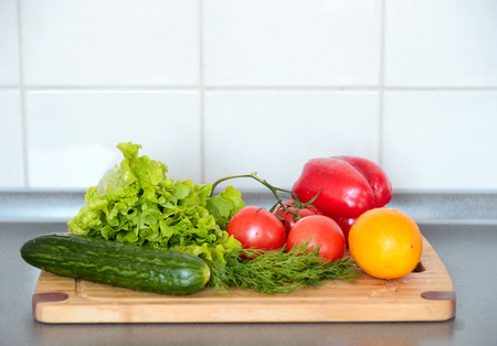 Vegetables, tomato, cucumber, salad, dill, bell pepper are on a wooden board in the kitchen.の写真素材