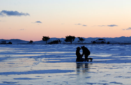 Silhouette of two men on the ice of a frozen lakeの写真素材