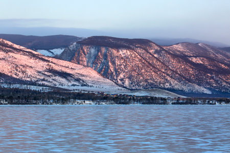 Winter landscape with frozen lake, mountains and forest in the background.の写真素材