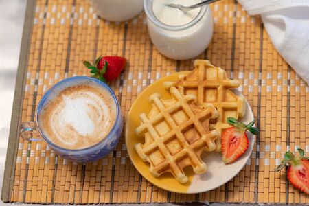 two baked Belgian Viennese waffles on the table with cappuccino and yogurt. breakfast in the...