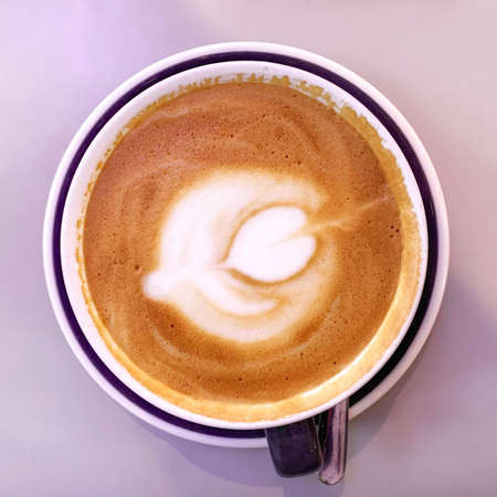 Dark cup of cappuccino with a pattern on the foam on a pink background. Top view.