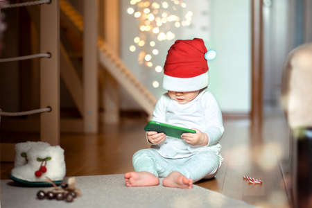 a baby up to a year old in a Santa costume looks at the phone with interest while sitting on the...